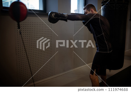 Intense workout of boxer practicing on floor-to-ceiling bag in gym 111974688