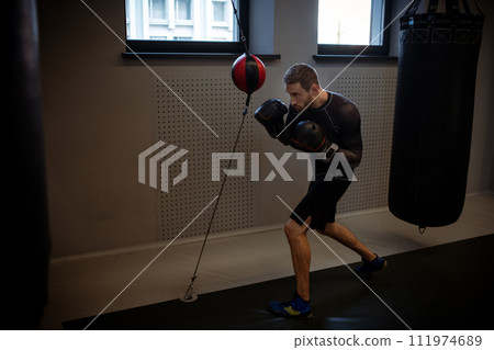 Boxer practicing coordination and punches on floor-to-ceiling bag in gym 111974689