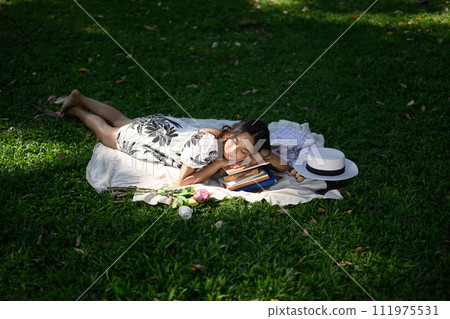 Calm young woman falling asleep on a stack of books, enjoys nature and sunny weather 111975531