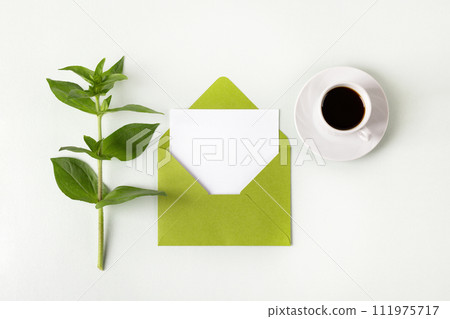 Green envelope with clean white sheet of paper for your text, cup of black coffee and leaves dahlias on gray background. Invitation to the holidays. Flat lay. Green envelope with clean white sheet of paper for your text, cup of black coffee and leaves dahlias on gray background. Invitation to the holidays. Flat lay. 111975717