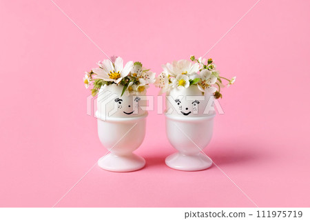 White eggs with funny face in a stand with spring pear and strawberry flowers on a pink background. Happy Easter White eggs with funny face in a stand with spring pear and strawberry flowers on a pink background. Happy Easter 111975719