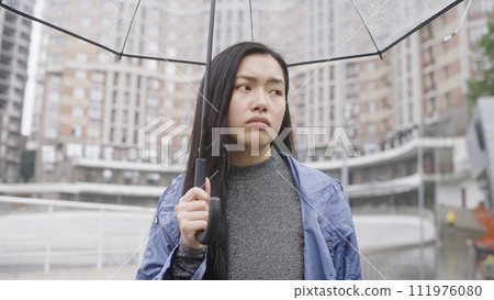 Brunette woman walking on street under rain with umbrella, bad mood, break-up 111976080