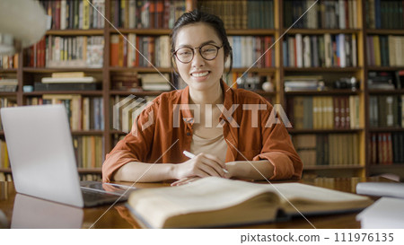 Portrait of happy asian woman student in the middle of studying process in the library Portrait of happy asian woman student in the middle of studying process in the library 111976135