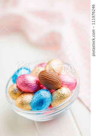 Easter chocolate eggs wrapped in aluminium foil in bowl on white table. 111976246