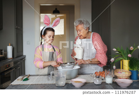 Grandmother with grandaughter preparing traditional easter meals, baking cakes and sweets. Passing down family recipes, custom and stories. 111976287