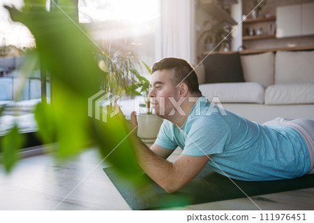 Young man with Down syndrome exercising at home, doing yoga, meditating. Man is praying, lying on belly. 111976451