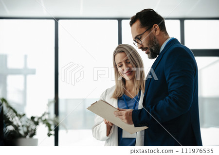 Pharmaceutical sales representative talking with female doctor in medical building. Hospital director consulting with healthcare staff. 111976535