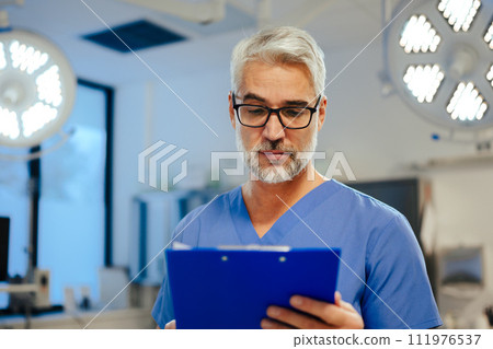Portrait of handsome male doctor in scrubs. ER doctor examining patient, reading medical test, lab results in clipboard. 111976537