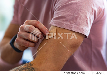 Young man putting nicotine patch on his shoulder, New Year's resolutions, quitting smoking, healthy lifestyle without cigarettes. Young man putting nicotine patch on his shoulder, New Year's resolutions, quitting smoking, healthy lifestyle without cigarettes. 111976549