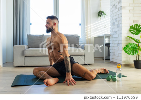 Handsome man doing yoga, stretching, resting after home workout, New Year's resolutions, exercising as healthy lifestyle and selfcare. Handsome man doing yoga, stretching, resting after home workout, New Year's resolutions, exercising as healthy lifestyle and selfcare. 111976559