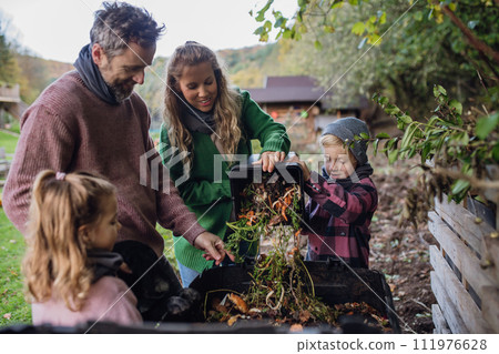 Family removing compost from a composter in garden, and composting kitchen waste in composter. Concept of composting and sustainable organic gardening. 111976628