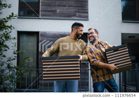 Man helping his friend move into new apartment in building. Man is moving into new flat, carrying box from the moving truck. 111976654