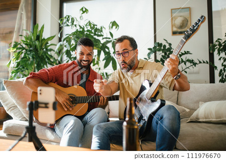 Best friends, musician jamming together, making video on social media. Playing music on guitar together at home for fans. Concept of male friendship, bromance. 111976670