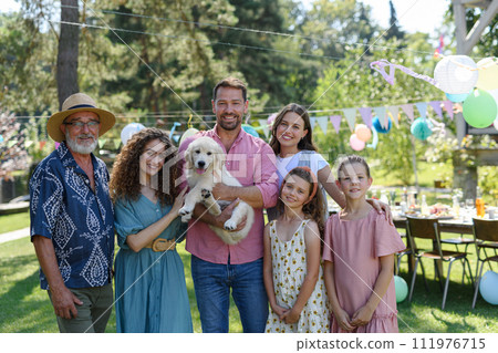 Family portrait at outdoor summer garden party. Family and friends standing, posing for a group photo. Multigenerational family. 111976715