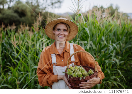 Female farmer holding harvest basket full of harvested corn. Concept of multigenerational and family farming. 111976741