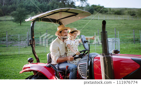 Farmer father riding tractor with his daughter. Girl growing up on family farm. Concept of multigenerational farming. Farmer father riding tractor with his daughter. Girl growing up on family farm. Concept of multigenerational farming. 111976774