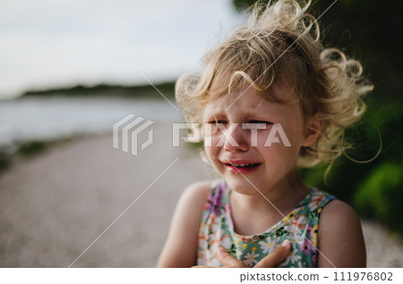Portrait of crying blonde girl in summer outfit on walk during summer vacation, concept of beach holiday. Portrait of crying blonde girl in summer outfit on walk during summer vacation, concept of beach holiday. 111976802