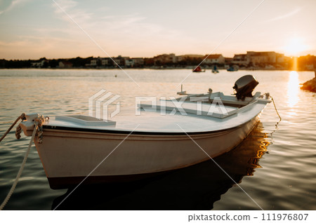Small boat on calm water, moored in the harbor during sunset. Small boat on calm water, moored in the harbor during sunset. 111976807