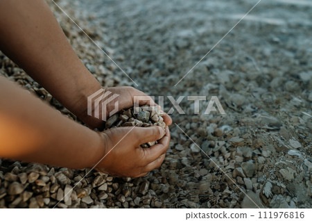 Close up of sea pebbles in boy's palms, pruney fingers. Seraching for shells in the sand. Concept of summer vacation by sea. Close up of sea pebbles in boy's palms, pruney fingers. Seraching for shells in the sand. Concept of summer vacation by sea. 111976816