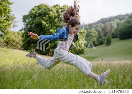 Beautiful young girl jumping in tall grass, having fun, enjoying warm spring day. 111976893