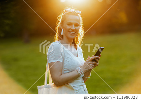 happy young 40 years old woman in white shirt using smartphone 111980328