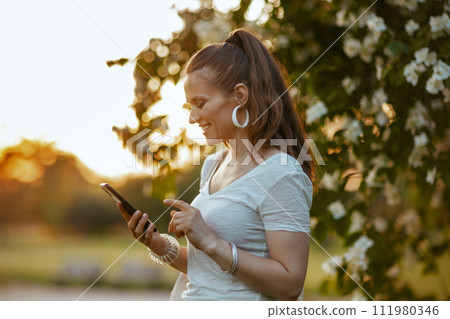 smiling trendy woman in white shirt using smartphone 111980346