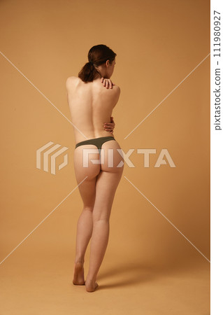 Full-length image of brunette young girl with slim, healthy, relief body, posing in cotton underwear against beige studio background 111980927