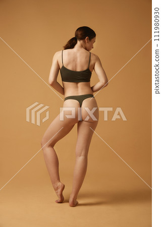 Full-length image of brunette young girl with slim, healthy, relief body, posing in cotton underwear against beige studio background Full-length image of brunette young girl with slim, healthy, relief body, posing in cotton underwear against beige studio background 111980930