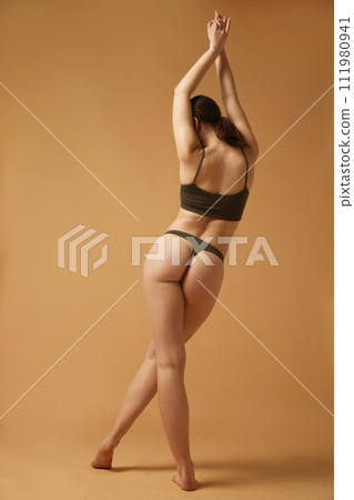 Well-being and body positive. Full-length image of slim, beautiful young woman with fit body standing in cotton underwear against beige studio background 111980941