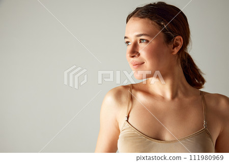 Portrait of beautiful smiling young girl with brunette hair in ponytail, posing in underwear against grey studio background 111980969