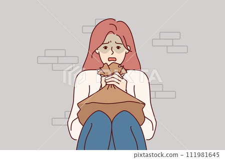 Woman suffering from panic attack holds paper bag for hyperventilation, sitting on floor near wall 111981645
