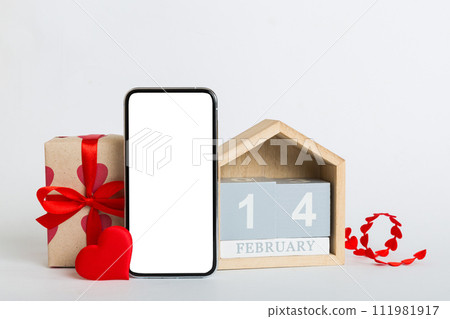 mobile phone with blank screen on colored background with hearts, calendar and gift box, valentine day 14 february concept perspertive view flat lay 111981917
