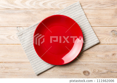 Top view on colored background empty round red plate on tablecloth for food. Empty dish on napkin with space for your design Top view on colored background empty round red plate on tablecloth for food. Empty dish on napkin with space for your design 111982006