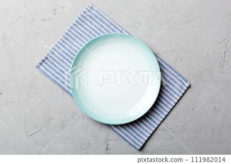 Top view on colored background empty round blue plate on tablecloth for food. Empty dish on napkin with space for your design Top view on colored background empty round blue plate on tablecloth for food. Empty dish on napkin with space for your design 111982014