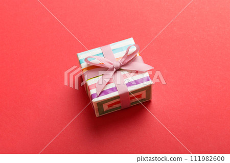 wrapped Christmas or other holiday handmade gift box in color paper with ribbon on colored background. Present box, decoration of gift on colored table, top view with copy space 111982600