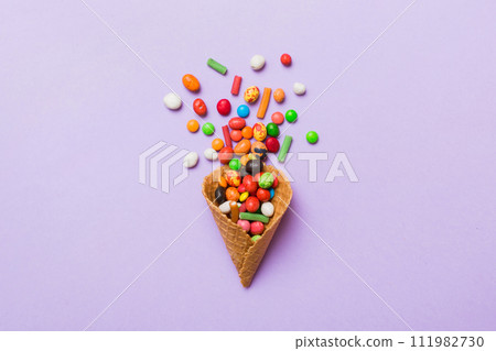 waffle cone full of assorted traditional candies falling out on colored background with copy space. Happy Holidays sale concept 111982730