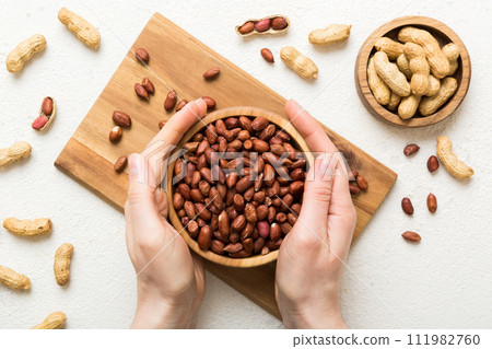 Woman hands holding a wooden bowl with peanuts. Healthy food and snack. Vegetarian snacks of different nuts Woman hands holding a wooden bowl with peanuts. Healthy food and snack. Vegetarian snacks of different nuts 111982760