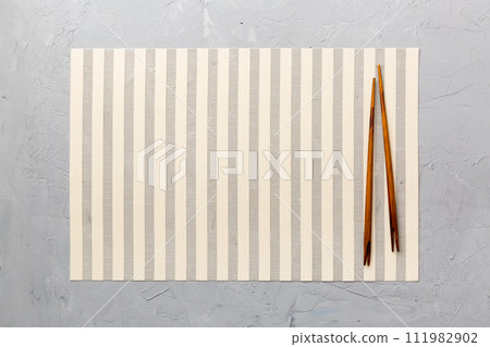 Two chopsticks and bamboo mat on cement background. Top view, copy space 111982902