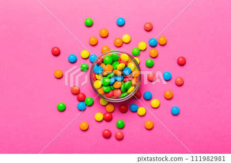different colored round candy in bowl and jars. Top view of large variety sweets and candies with copy space different colored round candy in bowl and jars. Top view of large variety sweets and candies with copy space 111982981
