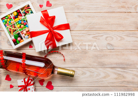Bottle of red wine on colored background for Valentine Day with gift and chocolate. Heart shaped with gift box of chocolates top view with copy space 111982998