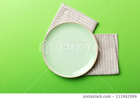 Top view on colored background empty round green plate on tablecloth for food. Empty dish on napkin with space for your design 111982999