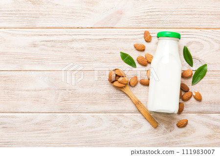 Top view of the almond milk in the glass bottle with almond nuts on the colored table. top view vith copy space Top view of the almond milk in the glass bottle with almond nuts on the colored table. top view vith copy space 111983007