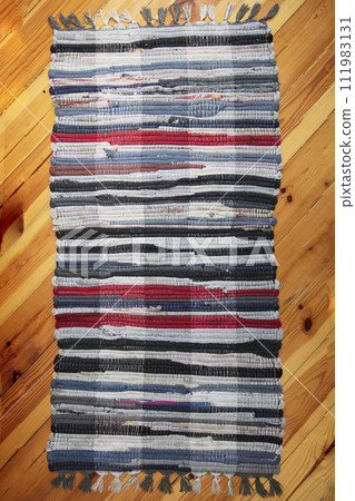 Rustic wicker rug on a wooden floor. Multi-colored Slavic carpet. Rustic wicker rug on a wooden floor. Multi-colored Slavic carpet. 111983131