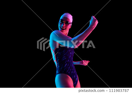 Portrait of happy, rejoice woman in swimsuit clenched fist in vibrant neon light against black studio background. Successful competition. Portrait of happy, rejoice woman in swimsuit clenched fist in vibrant neon light against black studio background. Successful competition. 111983787