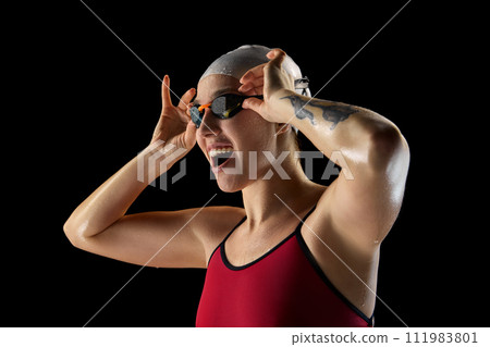 Portrait of young woman, skilled female swimmer with joyful facial expression against black studio background. Victory. 111983801