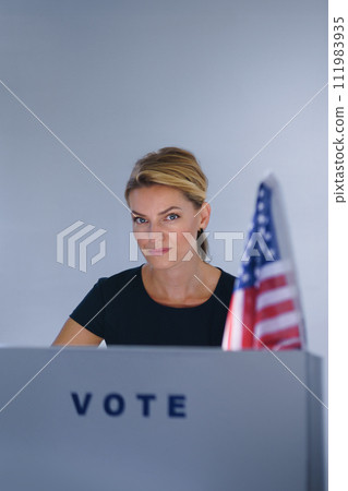 Portrait of female voter filling election ballot paper. US citizen voting in polling place on election day, usa elections. Portrait of female voter filling election ballot paper. US citizen voting in polling place on election day, usa elections. 111983935