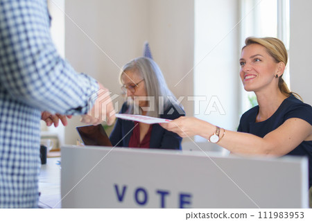 Member of electoral commission in polling place on election day, usa elections. Handing ballot. Member of electoral commission in polling place on election day, usa elections. Handing ballot. 111983953