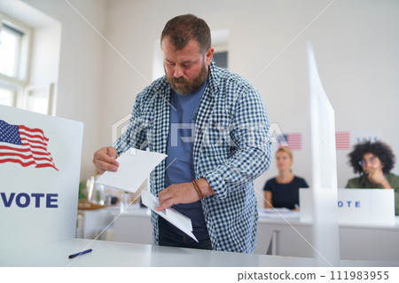 Male voter filling election ballot paper, putting his vote in the ballot box. US citizen voting in polling place on election day, usa elections. Male voter filling election ballot paper, putting his vote in the ballot box. US citizen voting in polling place on election day, usa elections. 111983955