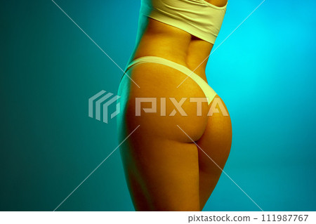 Cropped image of smooth, fit female buttocks. Model posing in cotton underwear against blue background in neon light. Anti-cellulite care Cropped image of smooth, fit female buttocks. Model posing in cotton underwear against blue background in neon light. Anti-cellulite care 111987767