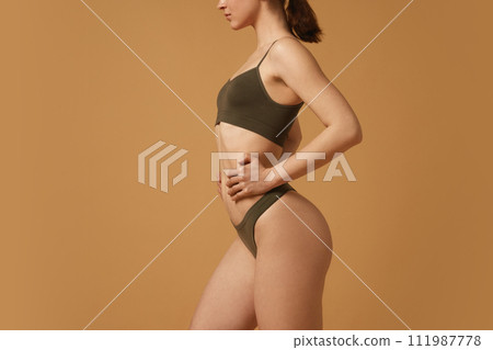Cropped image of fit female body, buttocks, slim waist. Model posing in cotton underwear against beige studio background. Body positive 111987778